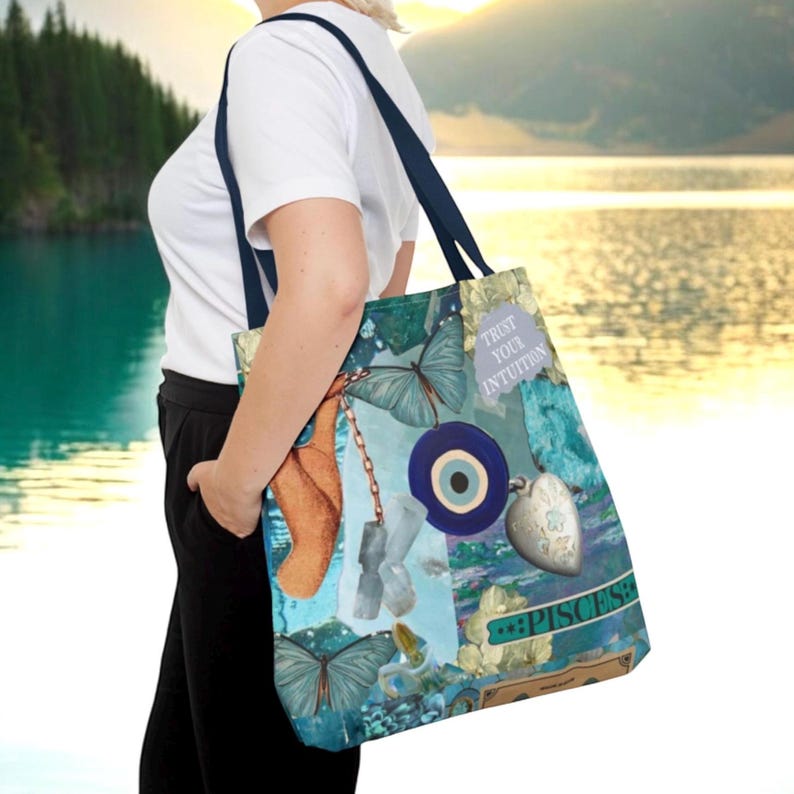 May include: A blue and teal tote bag with a butterfly and eye design. The bag has dark blue straps and features the text "Trust Your Intuition" and "Pisces". The bag is carried over the shoulder.