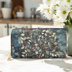 Könnte beinhalten: Eine rechteckige Geldbörse mit Reißverschluss, die einen dunkelblauen und blaugrünen Hintergrund im Aquarellstil mit einem zentralen Baummotiv zeigt. Der Baum hat komplexe Äste, die mit zahlreichen kleinen, bunten Blättern in Gold, Braun und Grün verziert sind.