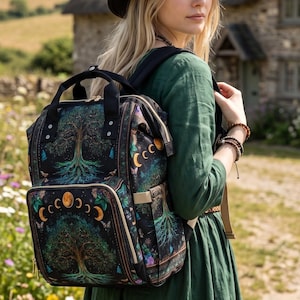 May include: A black backpack featuring a vibrant print of a tree with deep roots, surrounded by moon phases and small butterflies. The bag has a top handle, adjustable shoulder straps, and a front zippered pocket with gold-toned hardware accents.