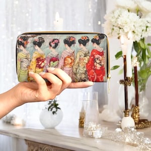 May include: A rectangular wallet with a gold zip is held up. The wallet features a colourful illustration of six women in traditional Japanese attire, each with a different kimono pattern. The background is a soft, muted blue.