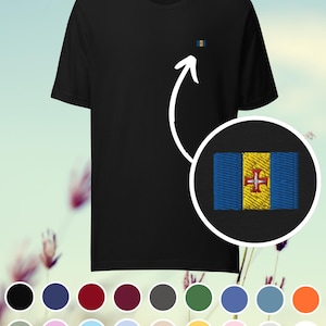 Puede incluir: Camiseta negra con una pequeña bandera bordada de Madeira, Portugal. La bandera presenta franjas verticales azules y amarillas con una cruz roja. Se muestra una paleta de colores de camisetas disponibles.