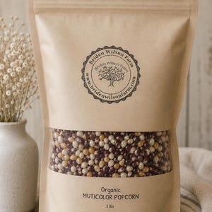 May include: A stand-up kraft paper pouch containing organic multicolor popcorn kernels. The label features the text Briden Wilson Farm and the website address. The lower portion of the bag is transparent, revealing the kernels. The bag is labeled 3 lbs.