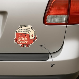 K&ouml;nnte beinhalten: Ein rot-cremefarbener Aufkleber mit dem Text "DON'T HATE ME BECAUSE I'M A Little Cooler" und einem Cartoon-K&uuml;hler-Design. Der Aufkleber ist etwa 13 cm gro&szlig;.