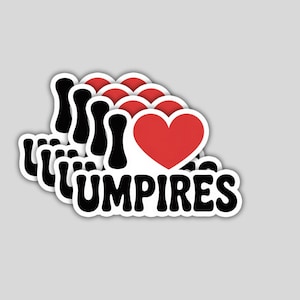 May include: A stack of stickers with the phrase "I love umpires" in black, with a red heart replacing the word "love". The stickers have a white border and are on a gray background.