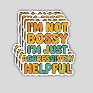 May include: A stack of stickers with the text "I'M NOT BOSSY I'M JUST AGGRESSIVELY HELPFUL" in orange, yellow, green, and blue. The stickers have a white border and a light gray background.