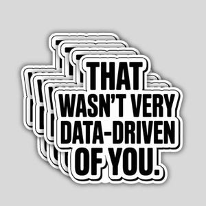 May include: A stack of white stickers with a black border. Each sticker has the text "THAT WASN'T VERY DATA-DRIVEN OF YOU!" in a bold, sans-serif font. The stickers are slightly overlapping, creating a layered effect.