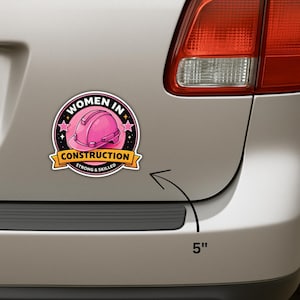 Puede incluir: Una pegatina redonda con el texto "WOMEN IN CONSTRUCTION" y un gr&aacute;fico de casco rosa. La pegatina tiene 12,7 cm de di&aacute;metro y tiene un borde negro con estrellas. El texto "STRONG & SKILLED" est&aacute; en una pancarta amarilla.