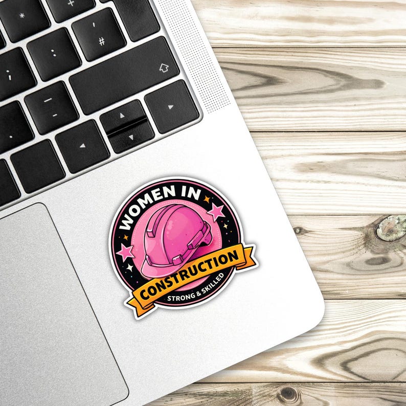 Puede incluir: Una pegatina con un casco de construcci&oacute;n rosa y el texto "WOMEN IN CONSTRUCTION" en un dise&ntilde;o circular. Debajo del casco hay una pancarta que dice "CONSTRUCTION STRONG & SKILLED". La pegatina est&aacute; en un port&aacute;til.