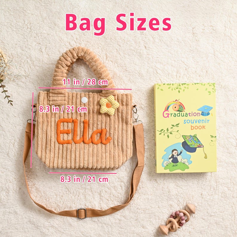 May include: A tan corduroy tote bag with the name "Ella" in orange, a yellow flower, and a detachable shoulder strap. The bag measures 11 inches wide and 8.3 inches high. A graduation souvenir book and a wooden toy are also in the image.