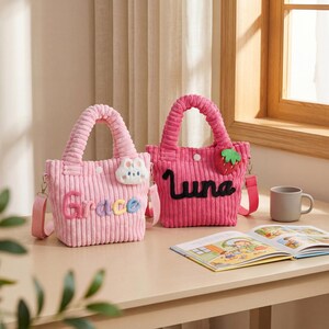 May include: Two pink corduroy tote bags with matching handles and shoulder straps. One bag has the name "Grace" embroidered in colorful letters, and a cloud and bunny applique. The other bag has the name "Luna" and a strawberry applique.