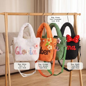 May include: Four corduroy tote bags in white, orange, green, and black hang on a wooden rack. Each bag has a different color strap and decorative elements, including floral accents and text. The bags are approximately 10 inches tall.