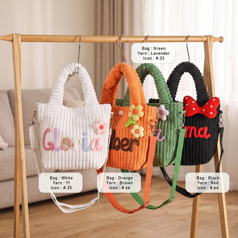 May include: Four corduroy tote bags in white, orange, green, and black hang on a wooden rack. Each bag has a different color strap and decorative elements, including floral accents and text. The bags are approximately 10 inches tall.