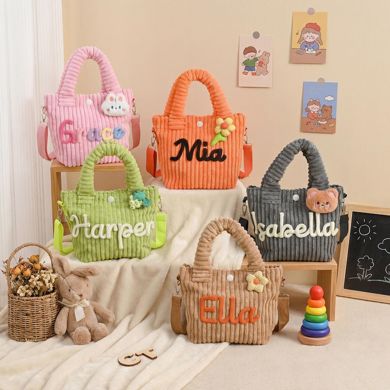 May include: Five corduroy tote bags in pink, orange, green, gray, and tan, each with a name embroidered on the front. The bags have matching handles and adjustable shoulder straps. Decorative accents include flowers and a bunny.
