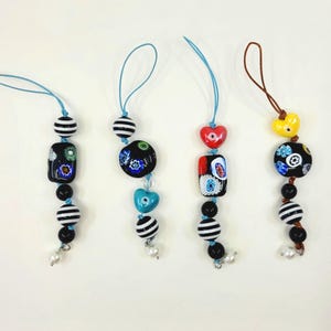 Può includere: Quattro ciondoli per telefono colorati con perline a righe bianche e nere, perline nere e perline in vetro di Murano. Ogni ciondolo ha una perlina a forma di cuore o quadrata di colore diverso.