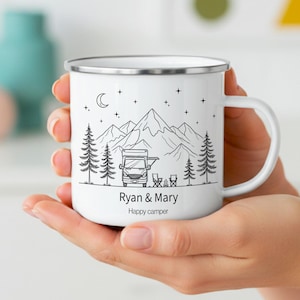 Può includere: Una tazza in smalto bianco con bordo argentato caratterizzata da un'illustrazione a linee nere di un camper, montagne, pini e stelle. Il testo Ryan & Mary e Happy camper è stampato in nero sotto l'illustrazione sulla parte anteriore.
