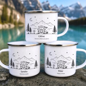 Pode incluir: Três canecas de esmalte branco com bordas prateadas, cada uma com uma ilustração de linha preta de um trailer, montanhas, árvores e uma lua crescente. As canecas são personalizadas com os nomes Céline, Sandra e Peter, junto com frases únicas.