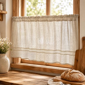 Peut inclure: Un rideau de fenêtre en lin beige avec un haut froncé et une bordure en dentelle décorative. Le rideau est suspendu devant un cadre de fenêtre en bois. Un vase de fleurs blanches est posé sur un comptoir en bois.