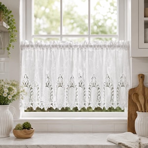 May include: A white cafe curtain featuring a delicate floral embroidery pattern on the upper section and a scalloped, intricate lace border along the bottom edge. The curtain is gathered on a rod, displaying a semi-sheer fabric texture.