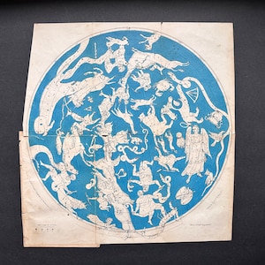 May include: Vintage celestial map featuring a blue background with white illustrations of constellations and figures. The map is circular, with detailed drawings of stars and celestial bodies. The paper has a worn, aged appearance.