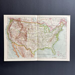 May include: Vintage map of the United States of America, open to display both sides. The map features states and geographical details in green, red, and brown. The title "United States of America" is visible.