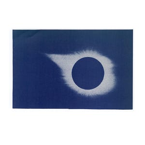 May include: A dark blue rectangular print featuring a white and gray depiction of a solar eclipse. The central dark circle is surrounded by a hazy, white corona effect, creating a striking contrast against the deep blue background.