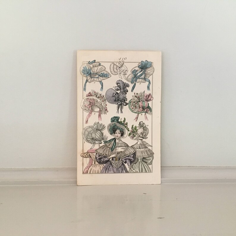 Puede incluir: Una ilustraci&oacute;n vintage de varios sombreros de mujer de la d&eacute;cada de 1800. Los sombreros est&aacute;n hechos de paja, encaje y cinta y est&aacute;n decorados con flores, plumas y otros adornos. La ilustraci&oacute;n est&aacute; impresa en una p&aacute;gina con el n&uacute;mero "410" en la parte superior.