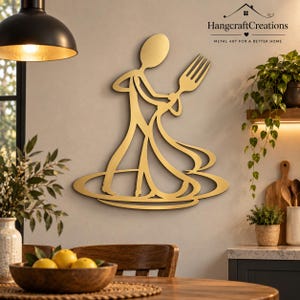 Op de afbeelding: Een goudkleurig metalen wandkunstwerk dat een gestileerde figuur met een grote vork voorstelt, met de tekst HangcraftCreations Metal Art for a Better Home in de rechterbovenhoek van de compositie.