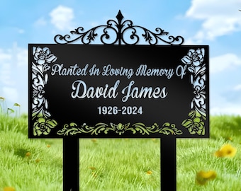 May include: Black metal garden sign with a decorative floral design. The sign reads "Planted in Loving Memory of David James 1926-2024".