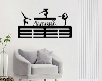 May include: Black metal gymnastics medal display with the name "Natasha" and three gymnast silhouettes. The display has 12 slots for medals.