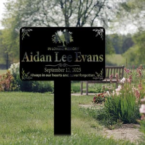 May include: Black metal memorial sign with a tree design and the text "IN LOVING MEMORY Aidan Lee Evans September 12, 2025 Always in our hearts and never forgotten."