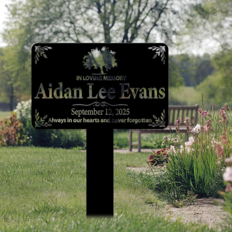 May include: Black metal memorial sign with a tree design and the text "IN LOVING MEMORY Aidan Lee Evans September 12, 2025 Always in our hearts and never forgotten."