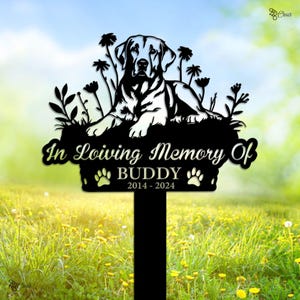 May include: Black metal memorial garden stake featuring a Labrador Retriever design. The stake reads "In Loving Memory Of BUDDY 2014-2024" with paw prints. The dog is lying down amidst stylized flowers and foliage.