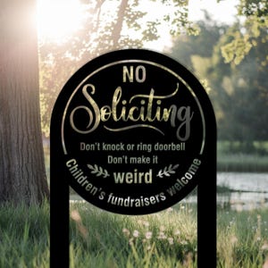 Puede incluir: Letrero de jardín de metal negro con las palabras "NO Soliciting" en una fuente decorativa. El letrero también incluye las frases "Don't knock or ring doorbell, Don't make it weird, Children's fundraisers welcome."