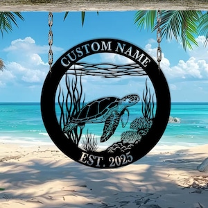 Op de afbeelding: Rond zwart metalen bord met een zeeschildpadontwerp. Het bord heeft de woorden "CUSTOM NAME" bovenaan en "EST. 2025" onderaan. De schildpad zwemt in de oceaan, omringd door zeewier en koraal. Het bord hangt aan kettingen.