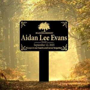 May include: Black metal memorial sign with a gold tree design and the text "IN LOVING MEMORY Aidan Lee Evans September 12, 2025 Always in our hearts and never forgotten."