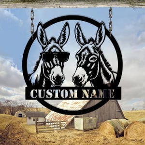 Puede incluir: Letrero de metal negro con dos cabezas de burro dentro de un círculo, una con gafas de sol. El letrero incluye el texto "CUSTOM NAME" en una pancarta. El letrero cuelga de cadenas.