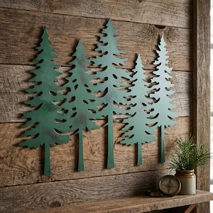 May include: A wall-mounted metal art piece featuring a silhouette of five evergreen trees in varying heights. The trees have a matte green finish with subtle dark shading and textured details, creating a layered forest scene on a flat surface.