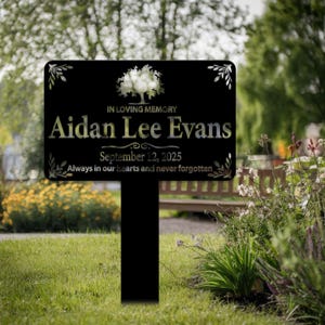 May include: Black metal memorial sign with a tree design and the text "IN LOVING MEMORY Aidan Lee Evans September 12, 2025 Always in our hearts and never forgotten."
