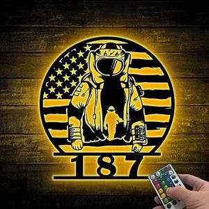 May include: A black and yellow metal wall art piece featuring an astronaut figure in front of an American flag design. The number "187" is displayed below the astronaut. A remote control is in the lower right corner.