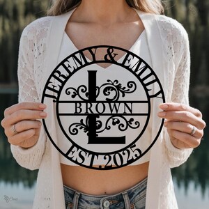 May include: Black metal sign with the names "Jeremy & Emily Brown" and the year "EST 2025" in a circle with a decorative floral design and the letter "L" in the center.