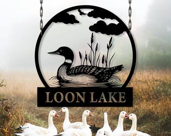 May include: Black metal Loon Lake sign with a loon silhouette inside a circle, hanging from chains. The sign includes the text "LOON LAKE" and is set against a blurred background of geese and a natural landscape.