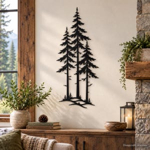 May include: A black metal wall art piece featuring a silhouette of three pine trees standing on a small mound. The design displays detailed branches and trunks, creating a vertical composition that is mounted on a plain, light-colored wall surface.