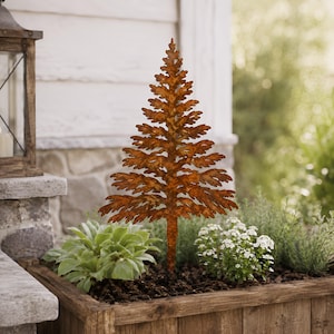 May include: A flat, two-dimensional metal cutout of a pine tree with a textured, rusted brown finish. The tree features a pointed top and layered, jagged branches that taper towards the base, designed as a decorative garden stake or ornament.