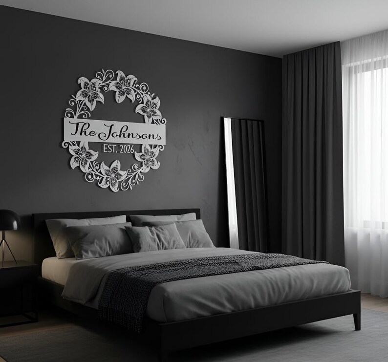 Puede incluir: Una corona floral de metal blanco con el texto "The Johnsons EST. 2026" montada en una pared gris oscuro sobre una cama. La corona presenta un dise&ntilde;o circular con detalles de flores y hojas.