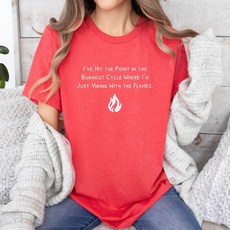 May include: Red t-shirt with the text "I'VE HIT THE POINT IN THE BURNOUT CYCLE WHERE I'M JUST VIBING WITH THE FLAMES." and a white flame graphic. The shirt is a crew neck style and has short sleeves.