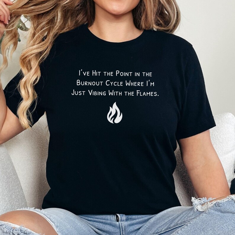 May include: Black t-shirt with white text that reads "I've Hit the Point in the Burnout Cycle Where I'm Just Vibing With the Flames." A white flame graphic is below the text. The shirt is a crew neck style.