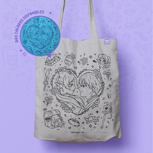 Puede incluir: Un bolso tote beige con una ilustración en blanco y negro de dos personas en forma de corazón, rodeadas de pequeños dibujos. El bolso tiene asas largas y una pequeña etiqueta. El texto "DOS COLORES DISPONIBLES" es visible.