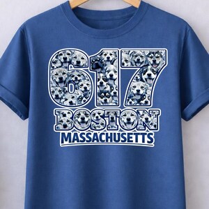 May include: A blue t-shirt with the number "617" in a white and blue design filled with dog faces. Below the number is the word "BOSTON" and "MASSACHUSETTS" in white text.