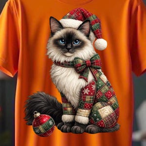 Puede incluir: Camiseta naranja con una ilustración de gato navideño. El gato lleva un gorro, bufanda y ropa de patchwork festivos. Una bola de Navidad está al lado del gato. La ilustración presenta ojos azules y un pelaje blanco y negro esponjoso.