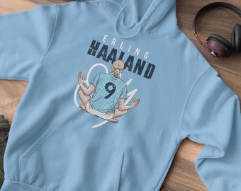 May include: Light blue hoodie featuring a graphic of a football player in a blue jersey with the number 9 on it. The text "Erling Haaland" is printed above the player.